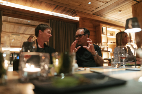 Zwei Gäste im Gespräch am Community Table, lachen und tauschen sich in gemütlicher Atmosphäre aus