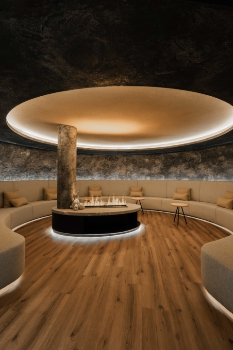 Runder Spa-Ruheraum mit zentralem Kamin, umlaufender Sitzbank, warmem Licht und stilvollem Design